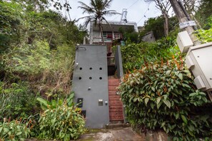 Un edificio residencial con fachada de concreto, una escalera de metal y una entrada protegida por vegetación densa.