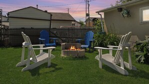 A backyard with a fire pit, two Adirondack chairs, and a wooden fence. - Family-friendly comfort near Misericordia Hospital and West Ed Mall (Edmonton)