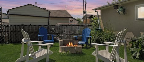 A backyard with a fire pit, two Adirondack chairs, and a wooden fence.