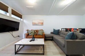 Een moderne woonkamer met een flatscreen televisie aan de wand, een salontafel met een vaas en twee banken met decoratieve kussens.