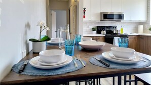 A modern kitchen with white cabinets, a microwave, and a stove. There is a dining table set with plates, bowls, and cutlery. - Family-friendly comfort near Misericordia Hospital and West Ed Mall (Edmonton)