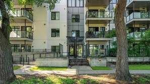 A multi-story residential building with balconies, a central entrance, and a small garden area.