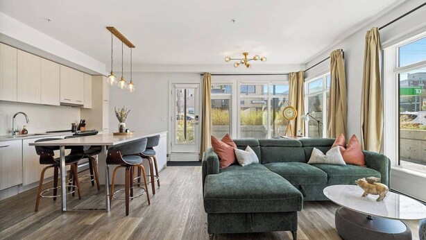 Een moderne woonkamer met een hoekbank, een eethoek met barstoelen en een keuken met een centraal kookeiland.