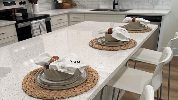 Cocina moderna con armarios blancos, encimera moteada y dos individuales tejidos con una nuez encima.