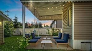 En overdækket terrasse med fire blå stole og et lille bord, omgivet af en græsplæne og et træstakværk.