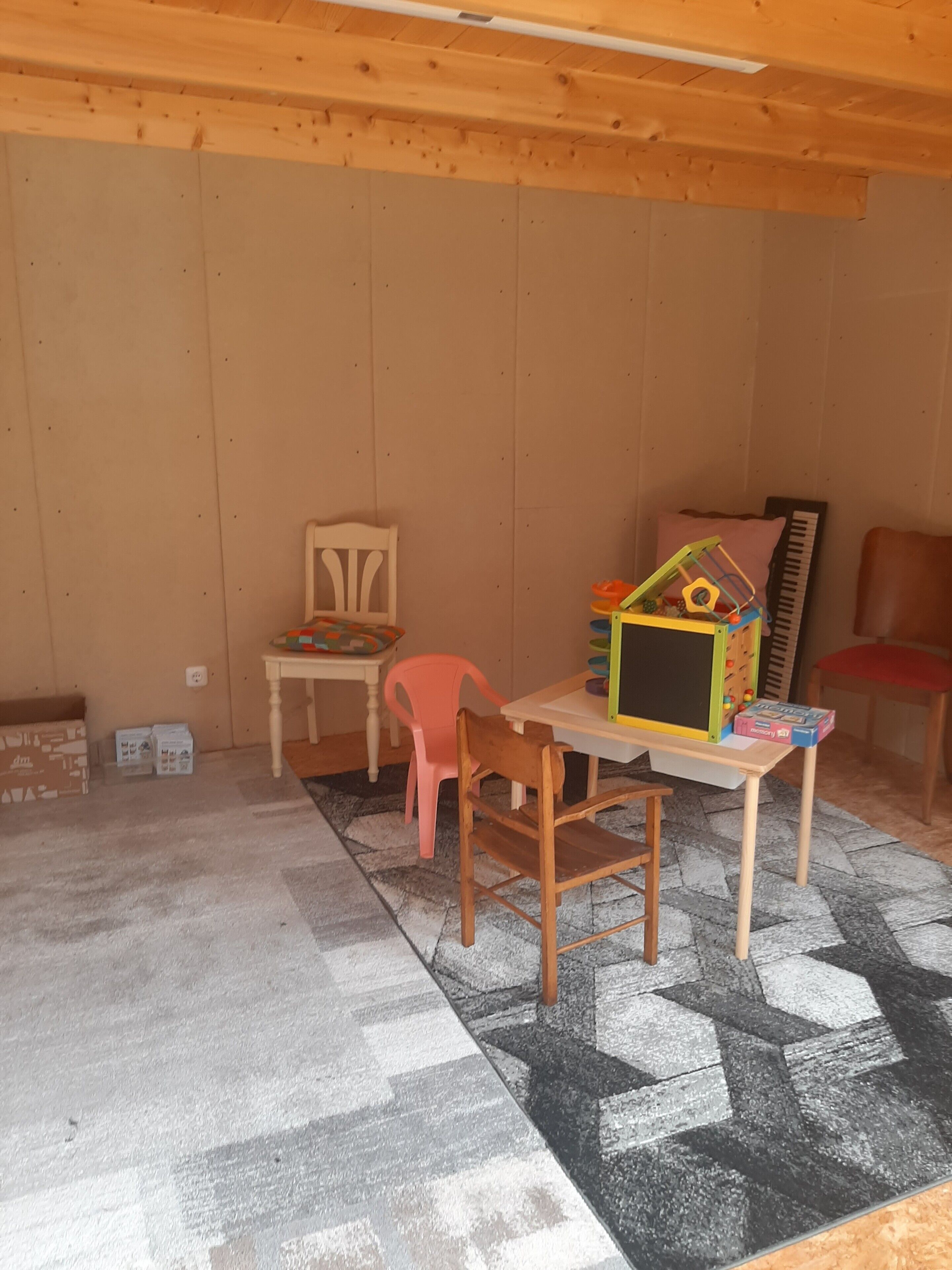 Ein Zimmer mit Holzboden, einem gemusterten Teppich, einem Holztisch mit Stuhl, einem pinken Sessel und einem Klavier.