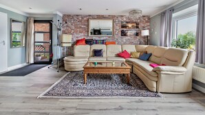 A living room with a brick wall, a beige sofa, a glass coffee table, and a patterned rug.