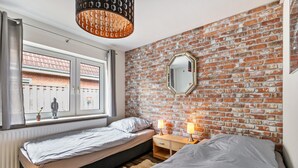 A bedroom with a brick wall, a window with a view, a bed, bedside tables, and a hanging light fixture.