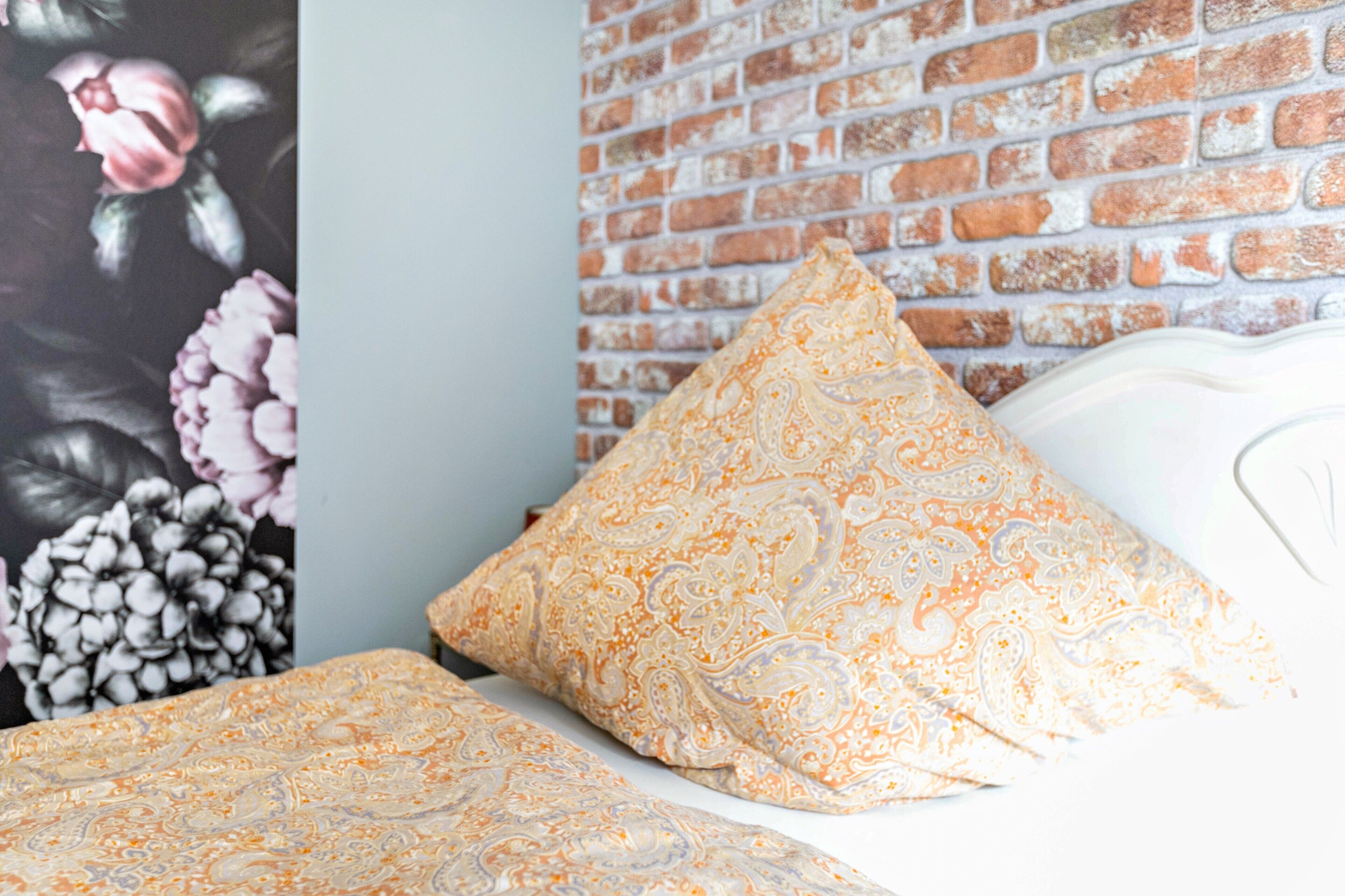 Cama com roupa de cama estampada, parede de tijolos e um mural floral.