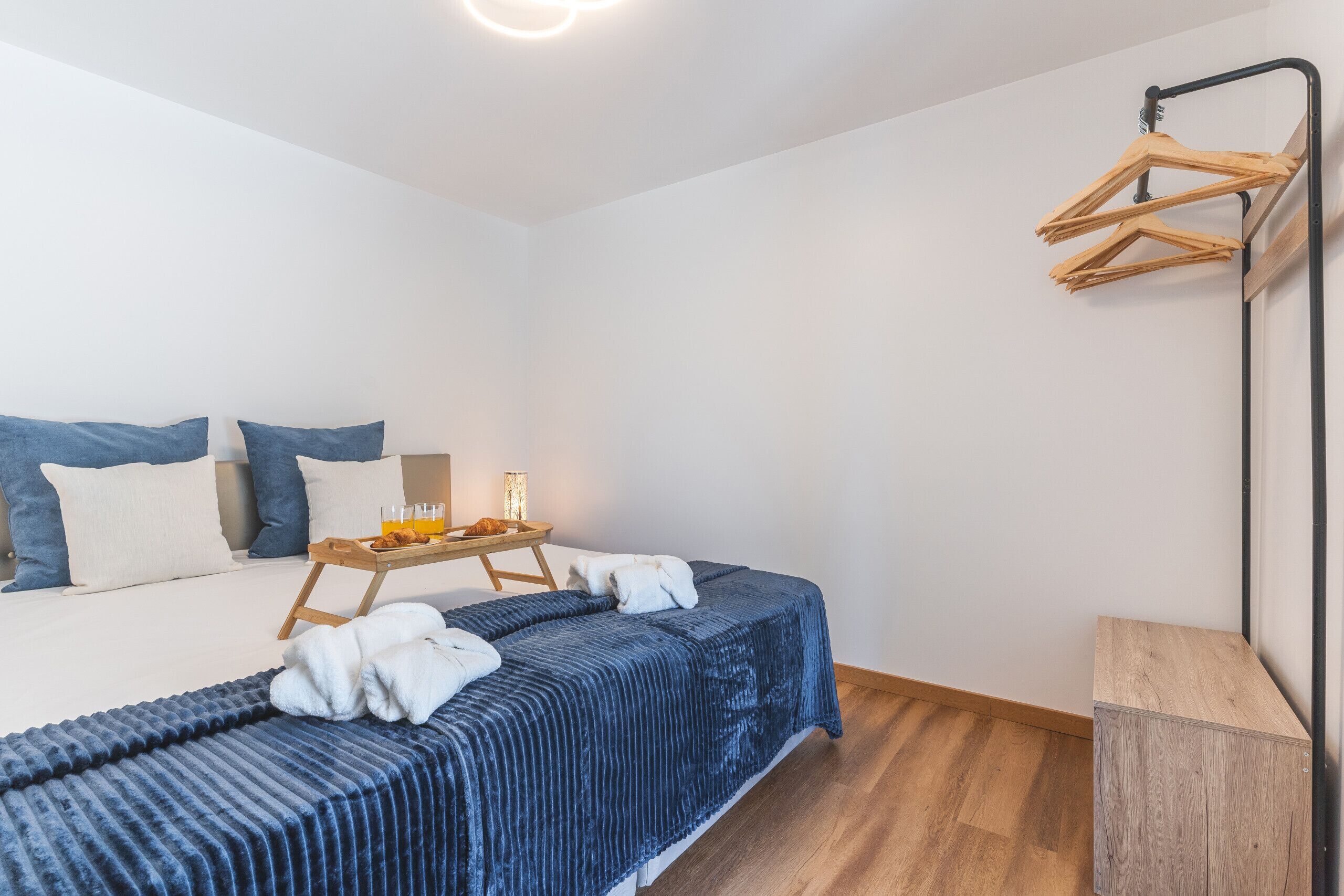 Une chambre bien rangée, avec un lit, une table de chevet et un portant à vêtements.