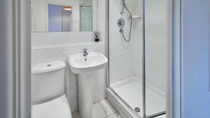 Een moderne badkamer met een douchecabine van glas, een wastafel op voetstuk en een toilet.