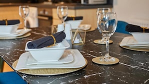 Een eettafel gedekt met witte borden, gevouwen servetten en heldere wijnglazen, met een moderne keuken op de achtergrond.