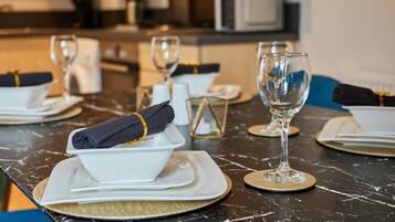 A dining table set with white plates, folded napkins, and clear wine glasses, with a modern kitchen in the background.
