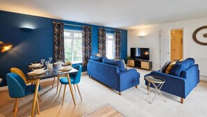Een moderne woonkamer met een eethoek, met blauwe banken, een eettafel voor vier personen en een televisie.
