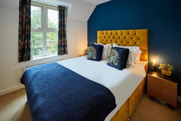 A bedroom with a large bed, a tufted headboard, and a window with curtains. - Hermitage Court Apartment in Leicester (Leicester)
