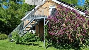 Una casa moderna con una escalera que lleva a un balcón, rodeada de exuberante vegetación y un cielo azul despejado.