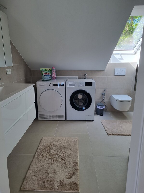 A compact laundry room with two washing machines, a toilet, and a skylight. - 90 m² apartment for 2 people in a newly renovated attic with a separate entrance (Schwentinental)