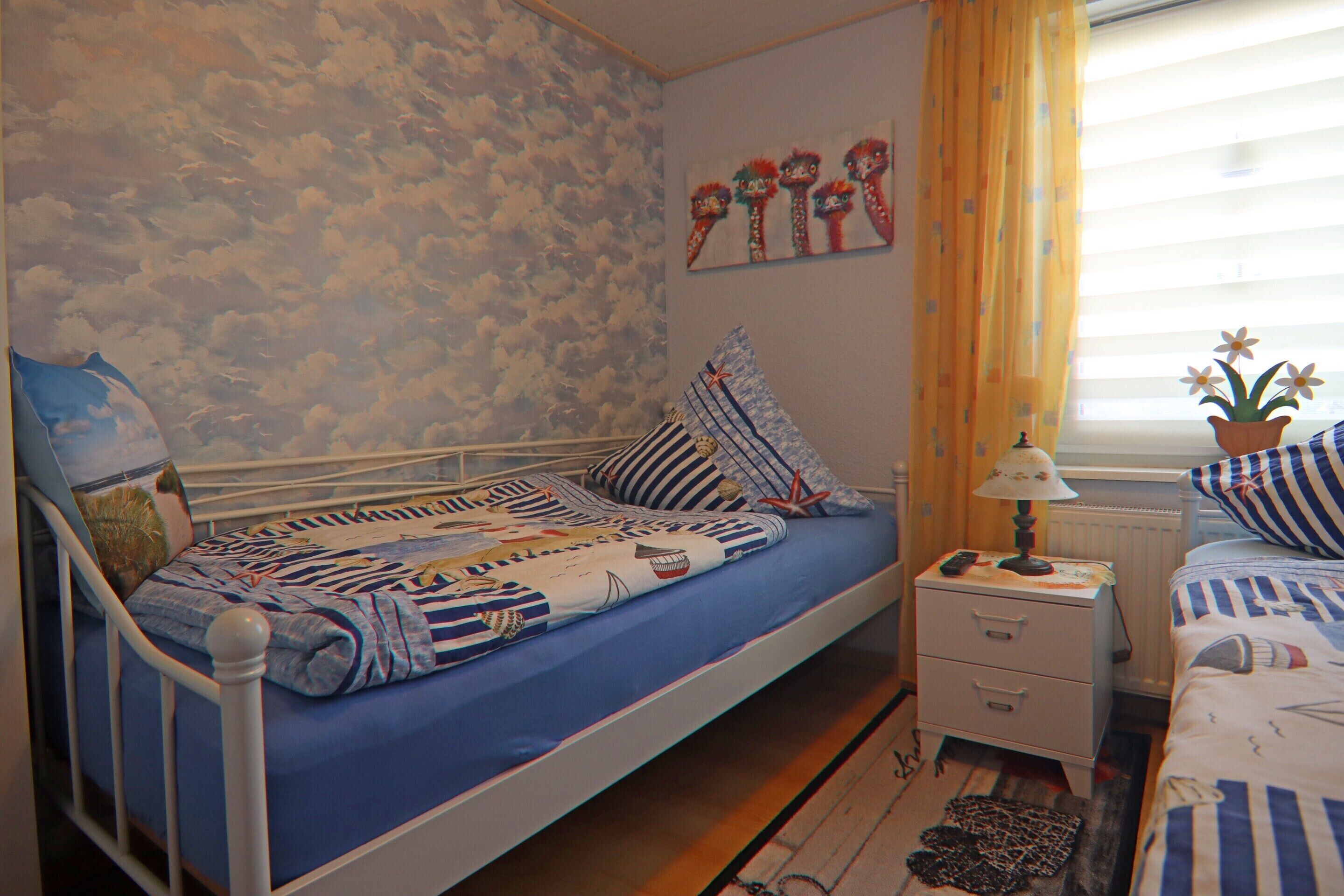 Un dormitorio con una cama individual, una mesita de noche, una lámpara y un ventanal con cortinas.