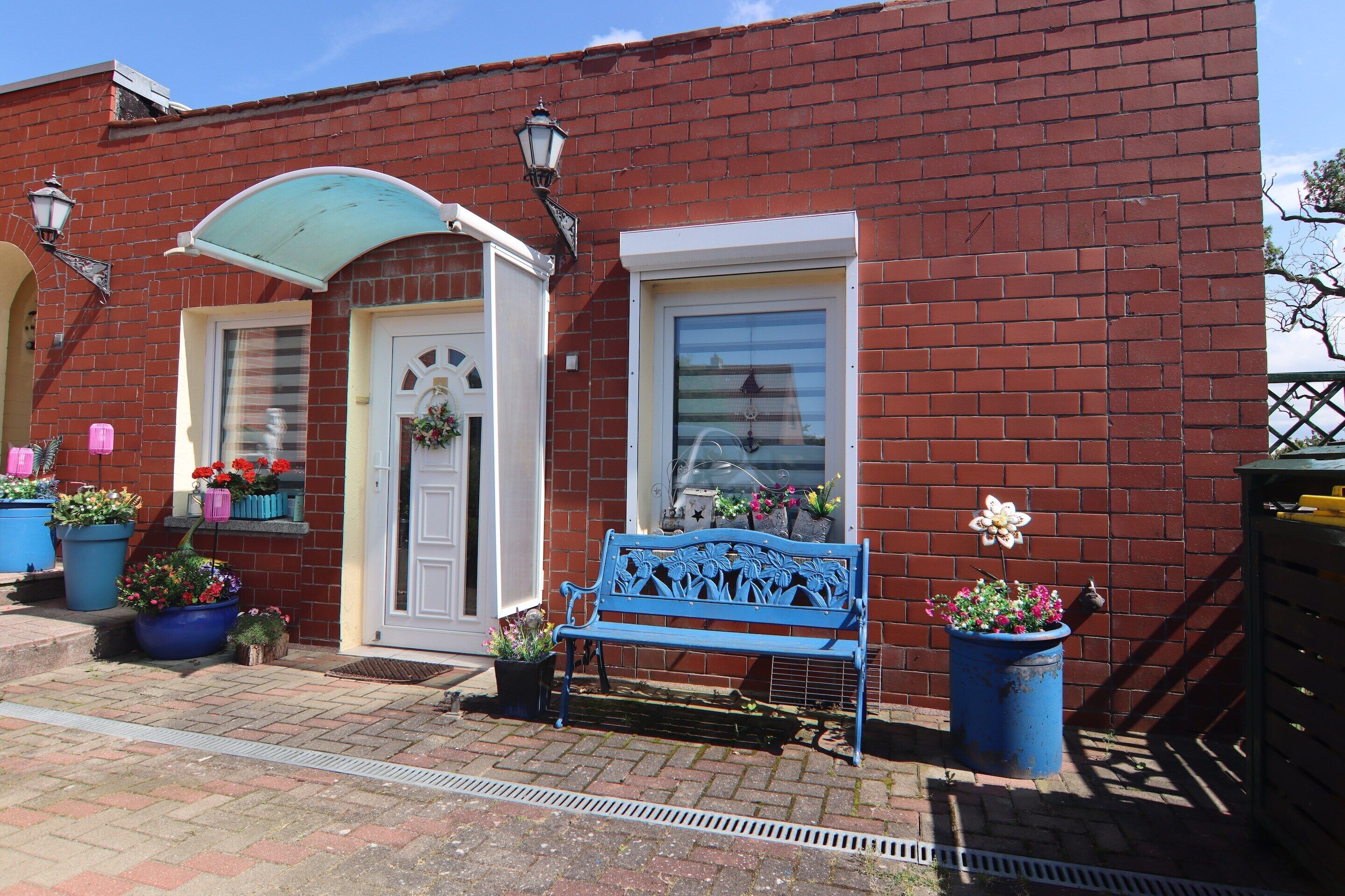 A red brick building with a white door, a blue bench, and potted plants.