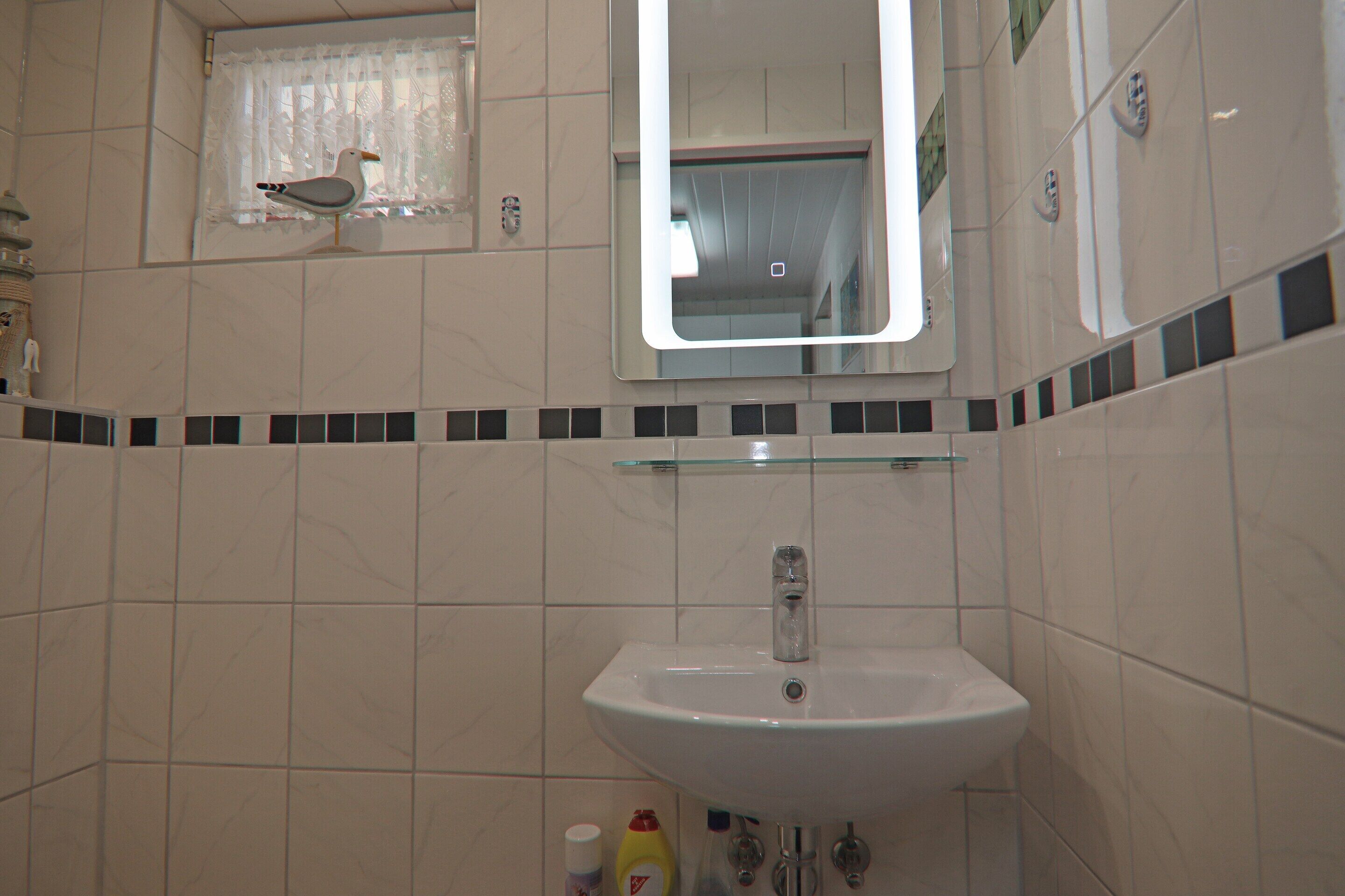 A bathroom with a white sink, a mirror, and a small window with a curtain.