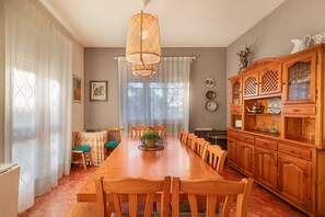 A dining room with a long wooden table, chairs, a hanging light fixture, and a wooden cabinet with glass doors.
