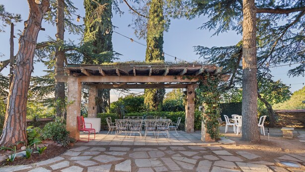 A stone patio with a pergola, outdoor seating, and surrounding trees. - Holiday Home 'Tordera Village' with Mountain View, Private Pool and Wi-Fi (Tordera)