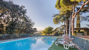 A swimming pool with a metal fence, surrounded by trees and a grassy area with lounge chairs. - Holiday Home 'Tordera Village' with Mountain View, Private Pool and Wi-Fi (Tordera)