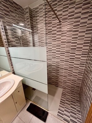 Un baño moderno con cabina de ducha de vidrio, un lavamanos blanco y un espejo.