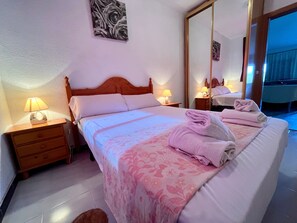 Habitación de hotel con cama, lámparas de noche, mesita de noche, espejo y baño visible a través de una puerta abierta.