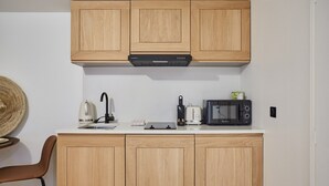 A compact kitchen with wooden cabinets, a microwave, a kettle, and a toaster.