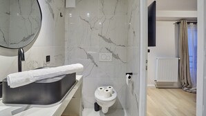A modern bathroom with a marble backsplash, a black sink, a toilet, and a shower area.