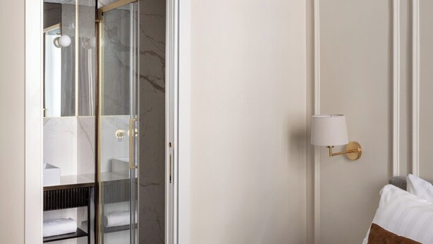 A hotel room with a bed, a bedside table, a lamp, a closet with a glass door, and a marble floor. - Golden House Vatican (Rome)