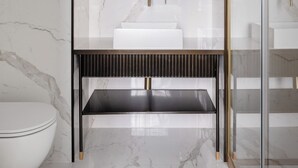 A modern bathroom with a marble wall, a glass-enclosed vanity, a white sink, and a gold faucet. - Golden House Vatican (Rome)