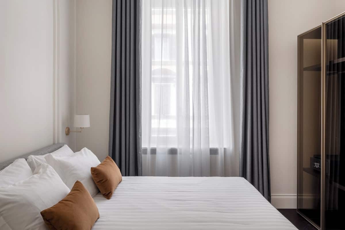 Ein Hotelzimmer mit Bett, weißer Bettwäsche, einem grauen Vorhang und einem Kleiderschrank.