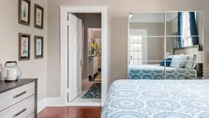 A bedroom with a bed, a dresser, a mirror, and a door leading to another room. - New Orleans Shotgun with private Patio (New Orleans)