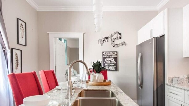 A modern kitchen with a marble countertop, stainless steel appliances, and red chairs at a dining table. - New Orleans Shotgun with private Patio (New Orleans)