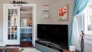 A living room with a television, a sofa, a coffee table, and a door leading to another room. - New Orleans Shotgun with private Patio (New Orleans)