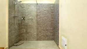 A small, enclosed shower area with a textured wall and a showerhead. - Independent suite in luxury guest house (Ngaparou)