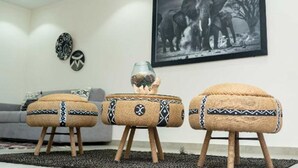 A living room with a grey sofa, three rattan poufs with black and white patterns, a framed black and white elephant photograph, and two wall-mounted decorative items. - Independent suite in luxury guest house (Ngaparou)