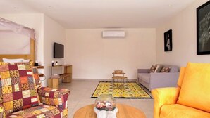 A living room with a sofa, armchair, coffee table, and a TV on a stand. - Independent suite in luxury guest house (Ngaparou)