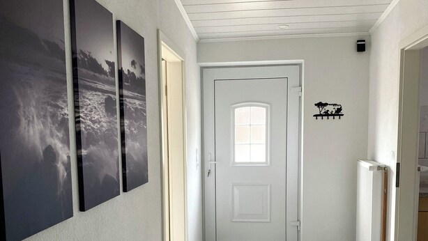 A hallway with a white door, a small window, and a wall-mounted shelf with a silhouette of a tree and people. - Vacations on a horse farm / vacation in the country, between Bremerhaven, HH and HB (Gnarrenburg)