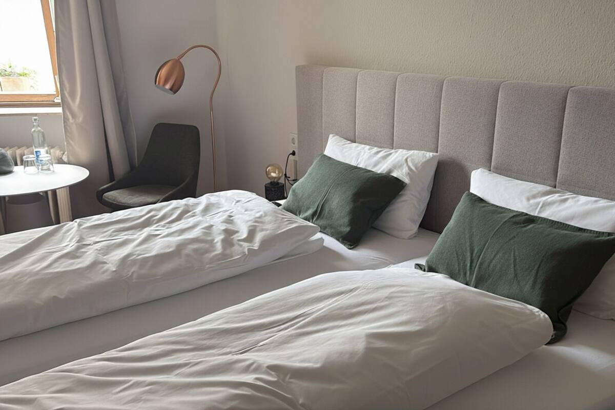 Ein Hotelzimmer mit zwei Betten, einem Sessel, einem Tisch und einer Lampe.