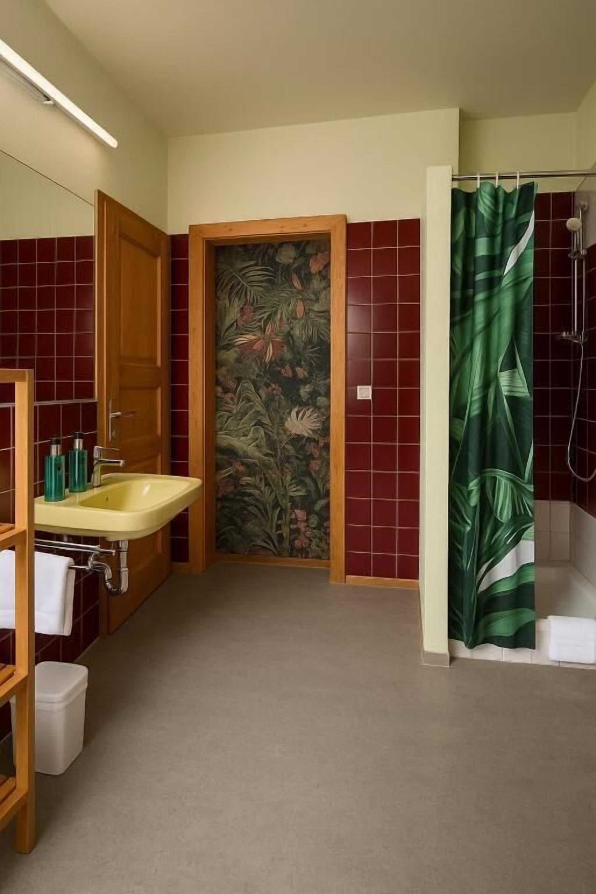 A bathroom with a yellow sink, a wooden door, and a shower curtain with a leaf pattern.