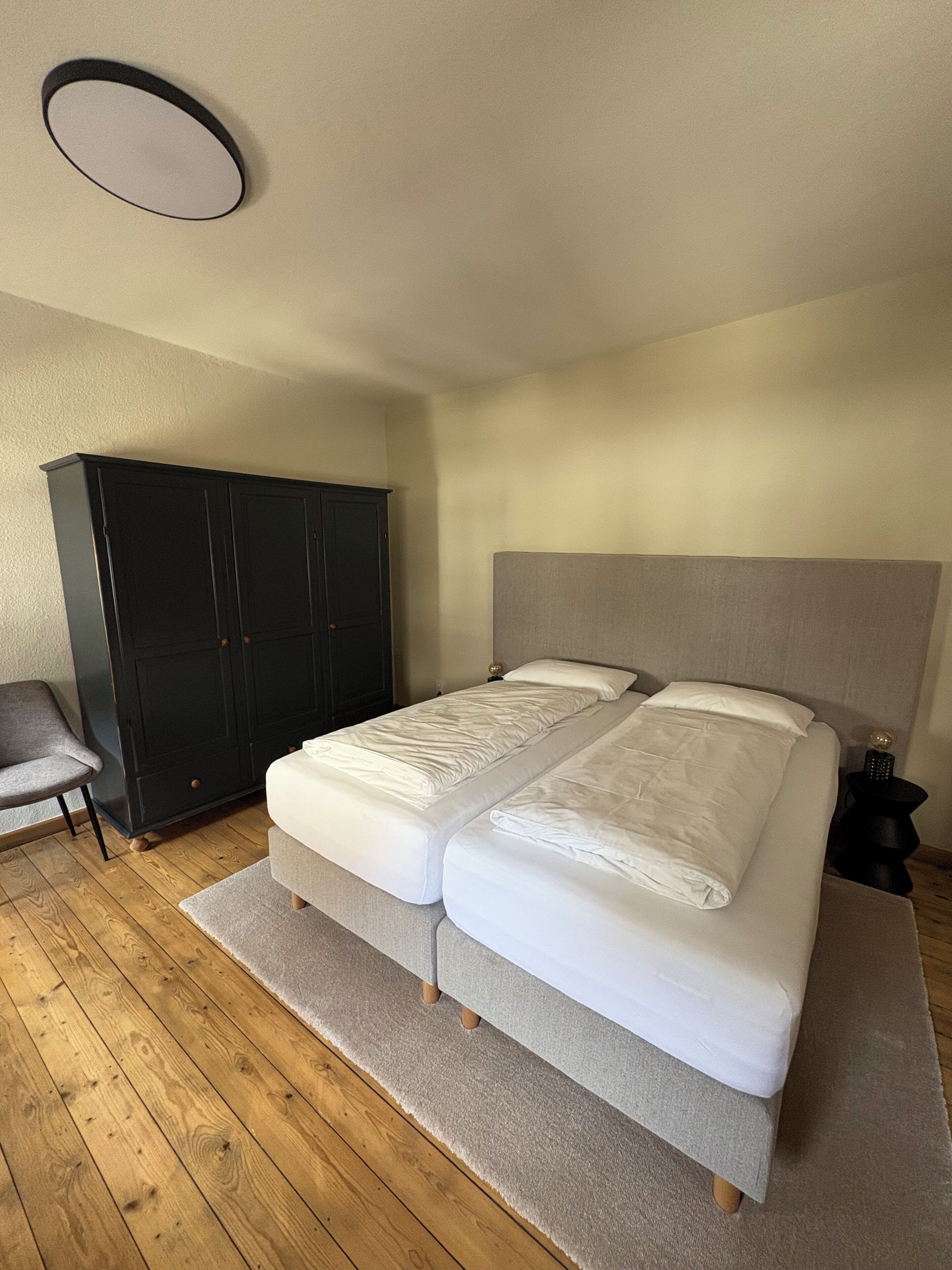 A bedroom with a double bed, a wardrobe, a chair, and a nightstand.