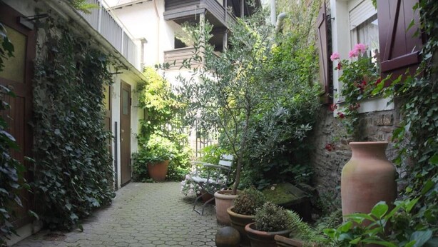 A narrow cobblestone pathway flanked by lush greenery and potted plants, leading to a building with a wooden bench and a rustic stone wall. - MYA Weinland Hotel Kobern-Gondorf (Kobern-Gondorf)