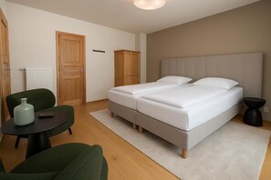 Ein Schlafzimmer mit zwei Betten, einem grünen Sessel, einem kleinen runden Tisch und einem Holzschrank.
