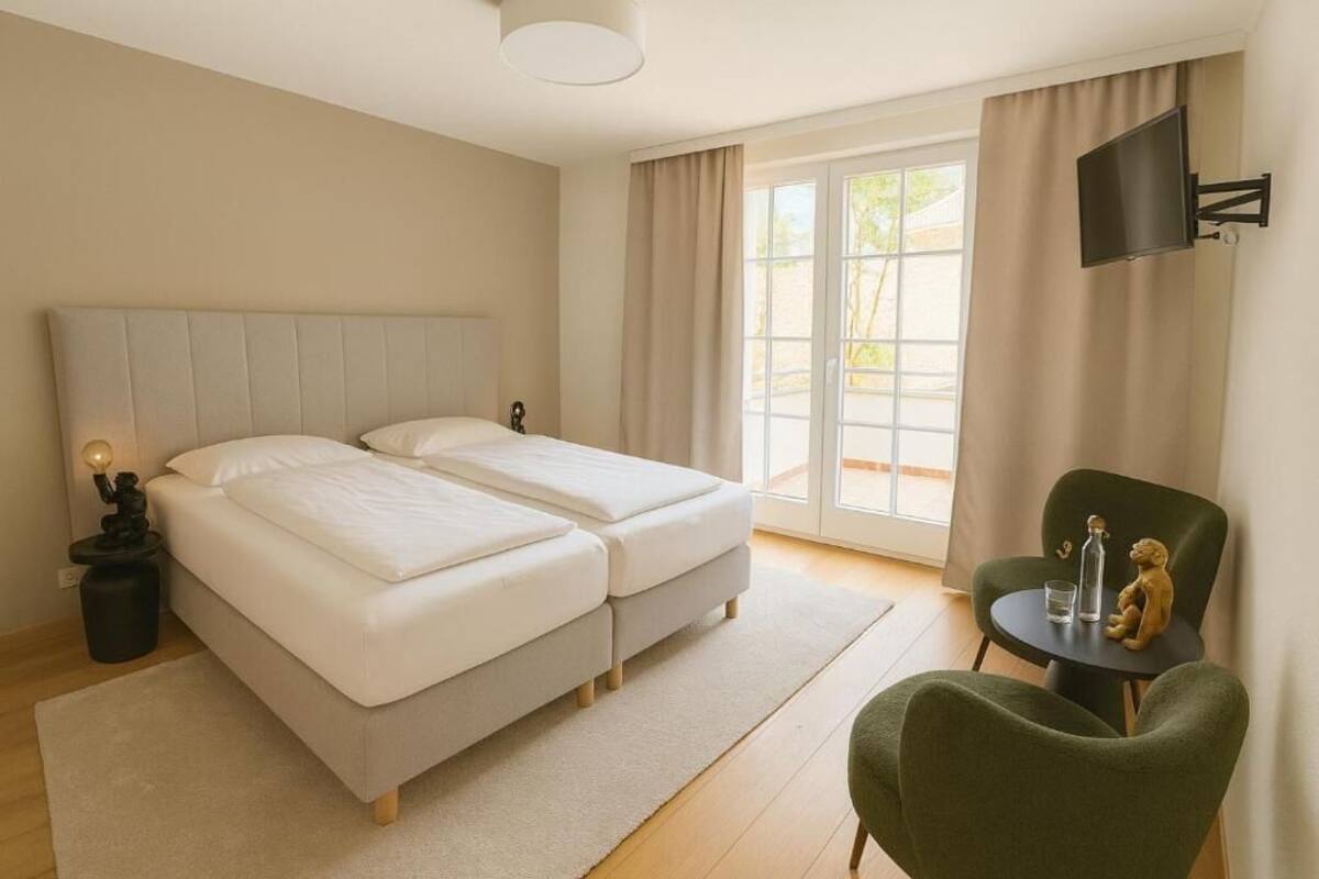 Ein Hotelzimmer mit zwei Betten, einem an der Wand montierten Fernseher, einem kleinen Tisch mit einer Statue und einem Stuhl.