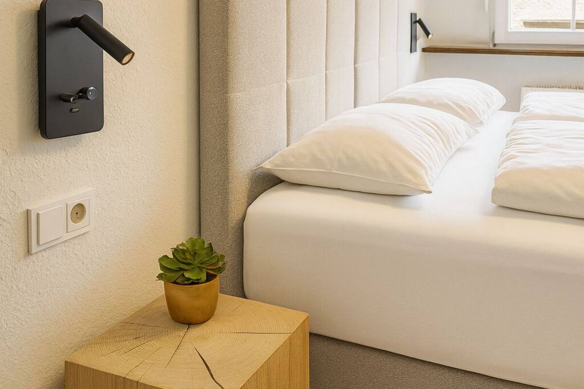 Ein Schlafzimmer mit einem Bett, einem Nachttisch mit Pflanze, einer Wandleuchte und gerahmten Bildern an der Wand.