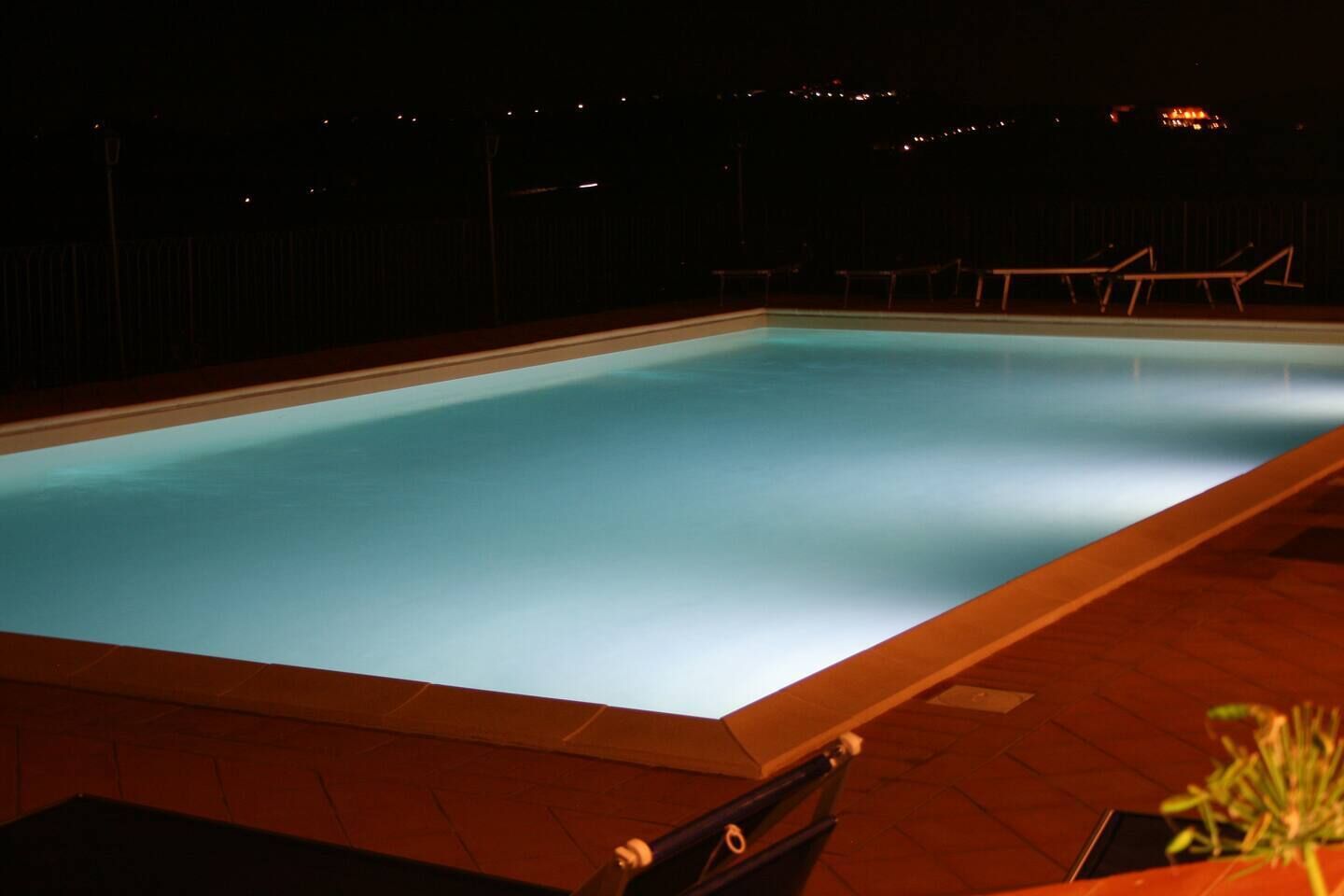 Et rektangulært swimmingpool med flisekant, omgivet af en træterrasse.