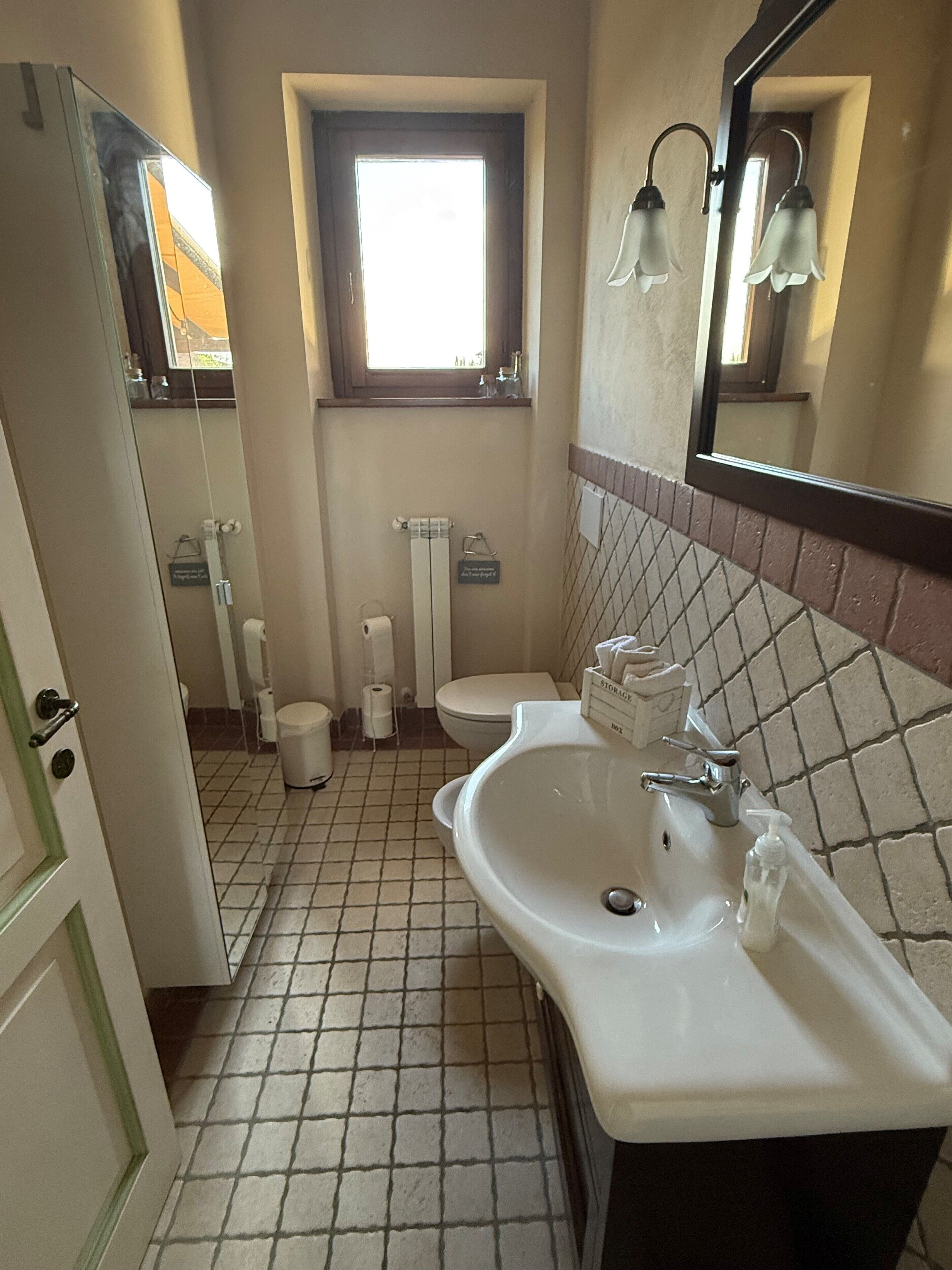 Un baño con lavamanos blanco, inodoro, ventana y espejo.